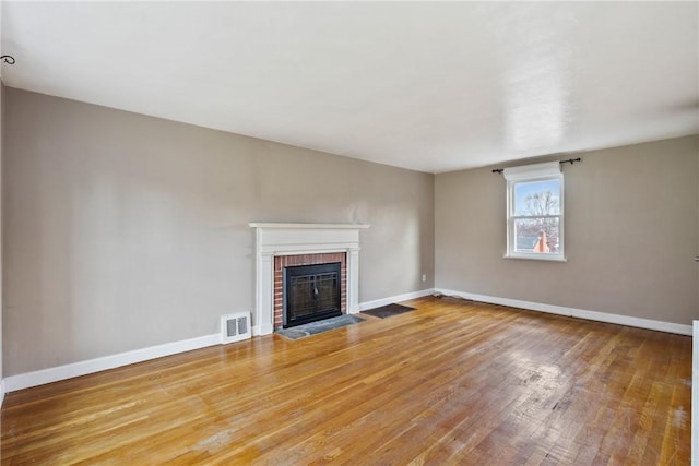 unfurnished living room featuring wood-type flooring and a brick fireplace