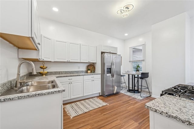 kitchen with sink, light hardwood / wood-style flooring, stainless steel refrigerator with ice dispenser, stove, and white cabinets