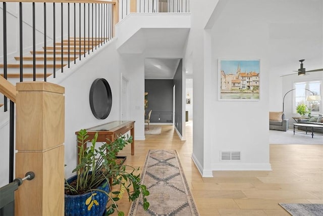 entryway featuring a towering ceiling, light wood-type flooring, and ceiling fan