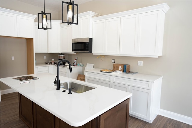 kitchen with white cabinets, decorative light fixtures, sink, and an island with sink