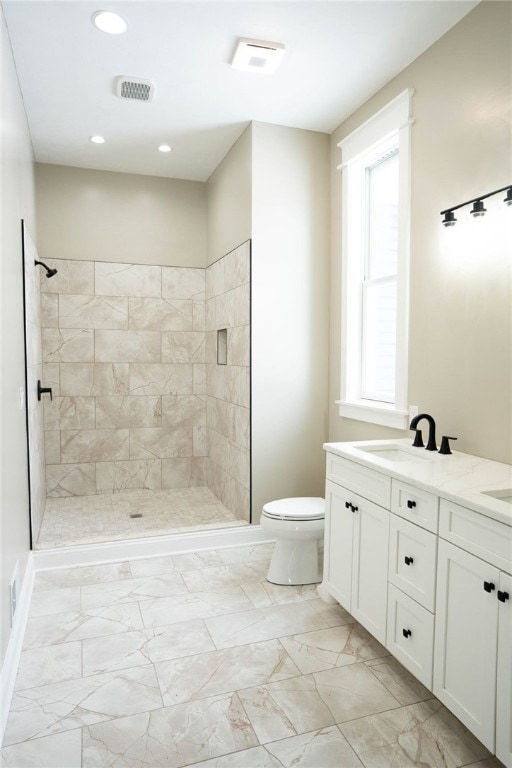 bathroom with a tile shower, vanity, toilet, and a wealth of natural light