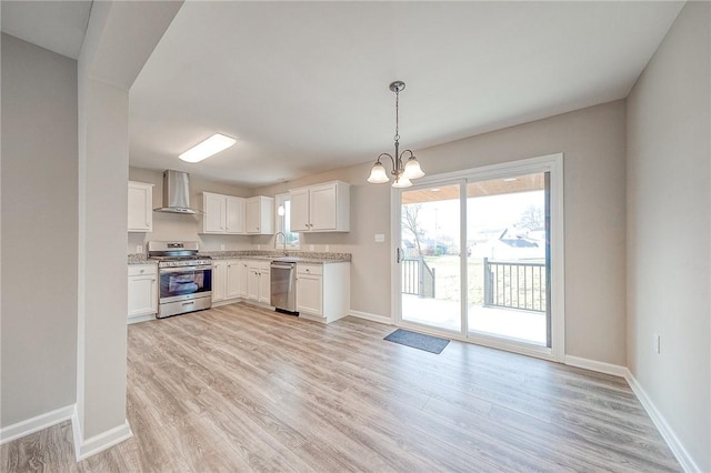 kitchen with appliances with stainless steel finishes, wall chimney range hood, decorative light fixtures, an inviting chandelier, and white cabinets