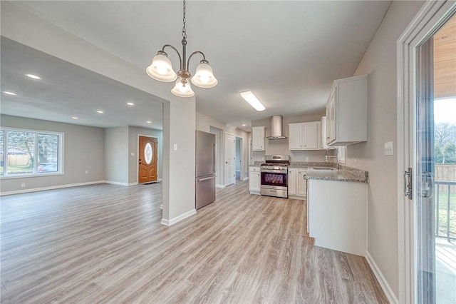 kitchen featuring white cabinets, wall chimney range hood, hanging light fixtures, sink, and appliances with stainless steel finishes