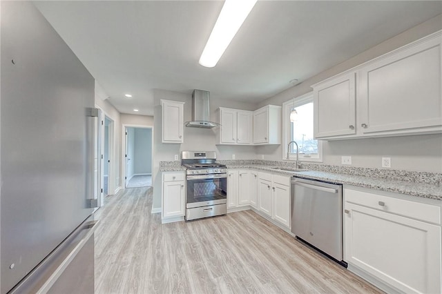 kitchen featuring appliances with stainless steel finishes, white cabinetry, wall chimney exhaust hood, and sink