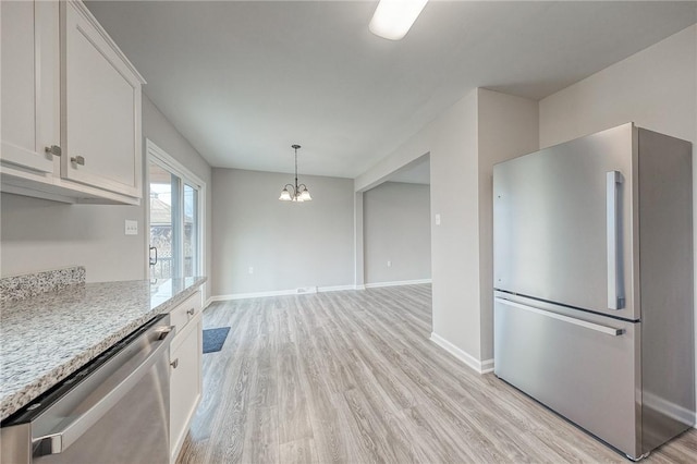 kitchen with light stone counters, white cabinets, a notable chandelier, and appliances with stainless steel finishes