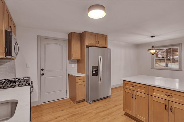 kitchen featuring tasteful backsplash, appliances with stainless steel finishes, light hardwood / wood-style floors, and pendant lighting