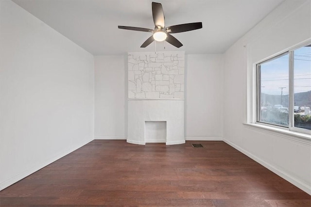 spare room featuring dark hardwood / wood-style floors, a stone fireplace, and ceiling fan