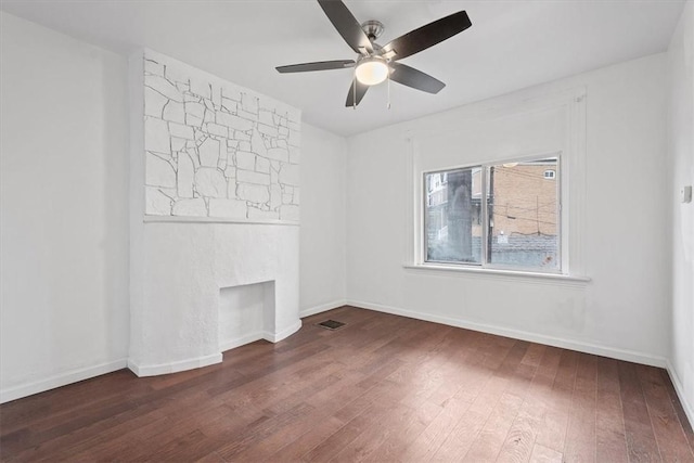 unfurnished room featuring dark hardwood / wood-style flooring, a stone fireplace, and ceiling fan