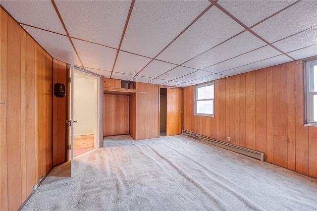 unfurnished bedroom featuring light carpet, a baseboard radiator, a drop ceiling, and wooden walls