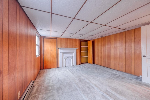 unfurnished living room featuring a drop ceiling, wood walls, light carpet, and a baseboard heating unit