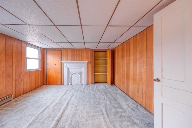 unfurnished living room with wood walls, light colored carpet, and a baseboard heating unit