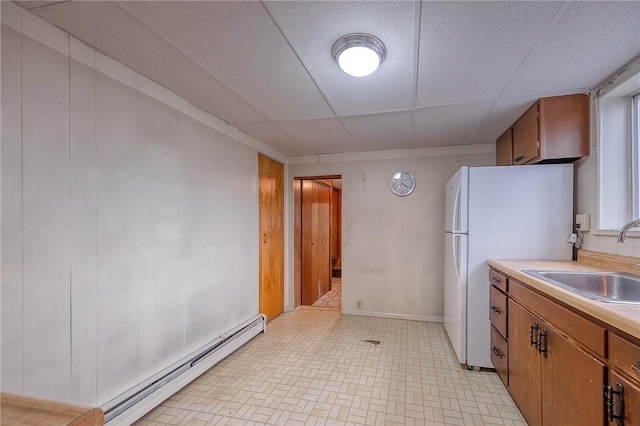 kitchen with white fridge, a drop ceiling, a baseboard heating unit, and sink