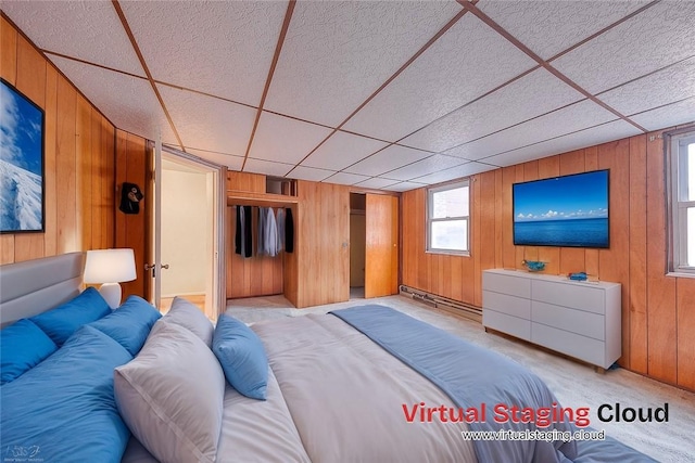 unfurnished bedroom with a drop ceiling, light carpet, wooden walls, and a baseboard heating unit