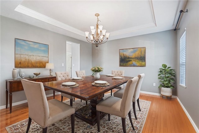 dining room with light wood-type flooring, a tray ceiling, and a notable chandelier