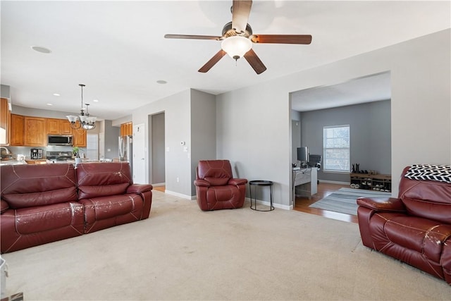 living room with ceiling fan with notable chandelier, sink, and light carpet