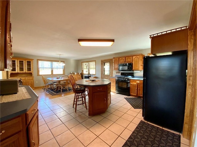 kitchen with light tile patterned floors, decorative light fixtures, a breakfast bar, a kitchen island, and black appliances