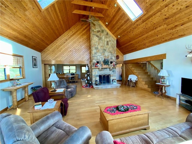 living room featuring high vaulted ceiling, a stone fireplace, a skylight, ceiling fan, and wood ceiling