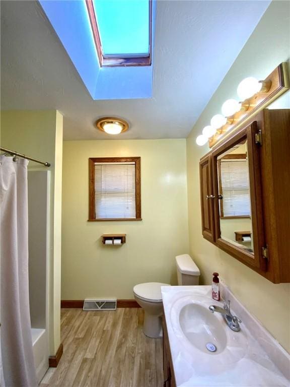 full bathroom featuring shower / bath combination with curtain, a skylight, vanity, hardwood / wood-style floors, and toilet