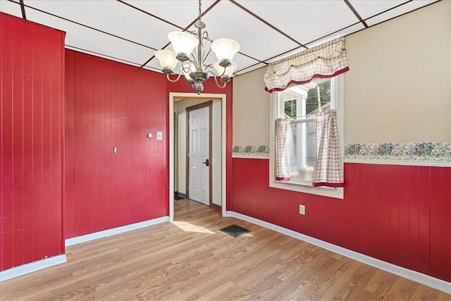 unfurnished dining area featuring a paneled ceiling, light hardwood / wood-style floors, and an inviting chandelier