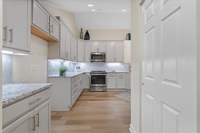 kitchen with stainless steel appliances, tasteful backsplash, light stone counters, light hardwood / wood-style floors, and lofted ceiling