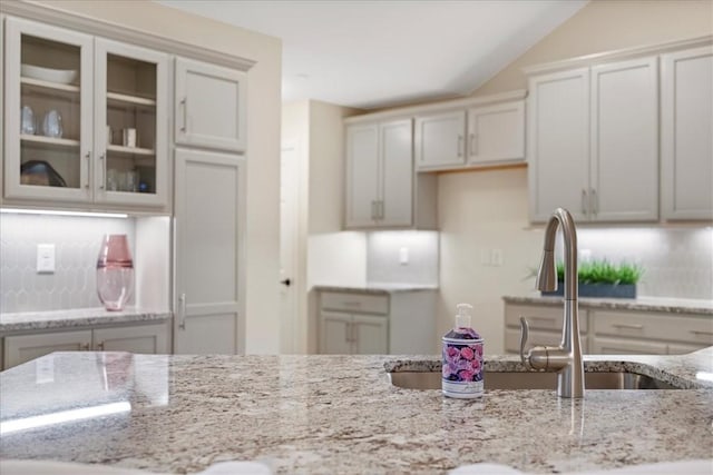 kitchen with lofted ceiling, sink, light stone countertops, tasteful backsplash, and white cabinetry