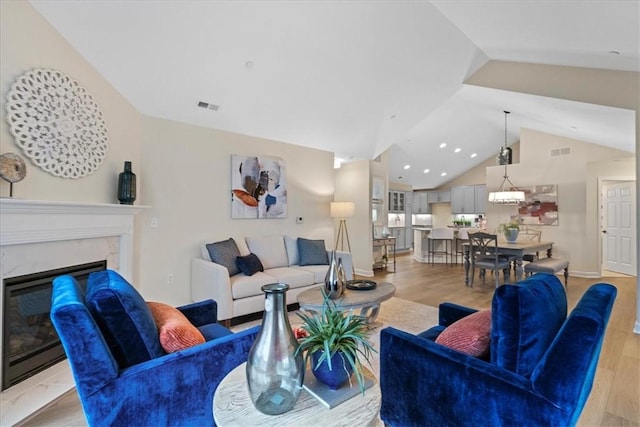 living room featuring light wood-type flooring, a premium fireplace, and vaulted ceiling