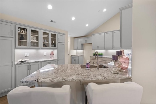 kitchen with light stone countertops, backsplash, a breakfast bar, sink, and gray cabinets