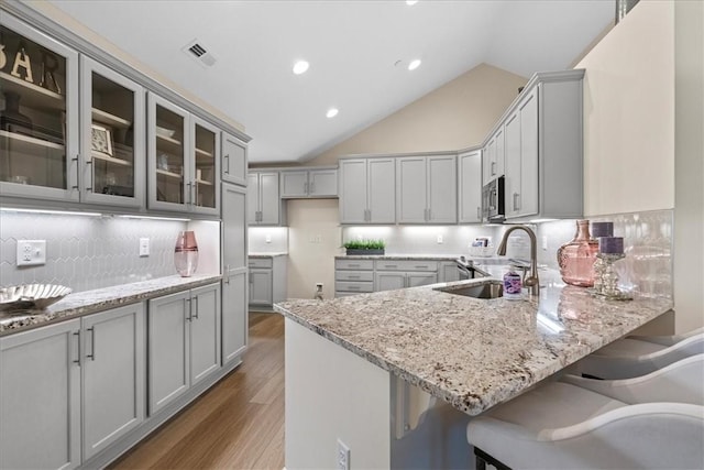 1111 Forest Oaks Dr, Center Twp, PA 16001 - kitchen featuring a peninsula, light stone counters, gray cabinetry, light wood-type flooring, and a kitchen breakfast bar