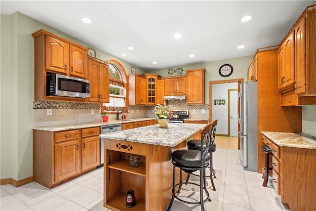 kitchen with light stone counters, light tile patterned flooring, a breakfast bar area, a kitchen island, and appliances with stainless steel finishes