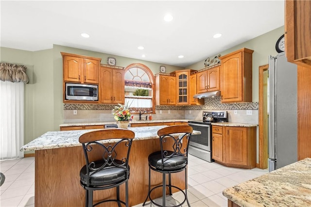 kitchen featuring a center island, a kitchen breakfast bar, decorative backsplash, light tile patterned floors, and appliances with stainless steel finishes