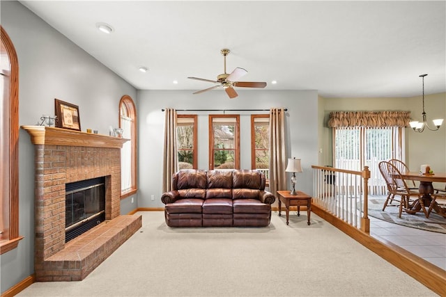 living room with ceiling fan with notable chandelier, carpet floors, and a brick fireplace