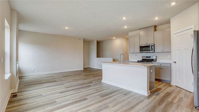 kitchen featuring gray cabinetry, stainless steel appliances, light hardwood / wood-style floors, sink, and a center island with sink