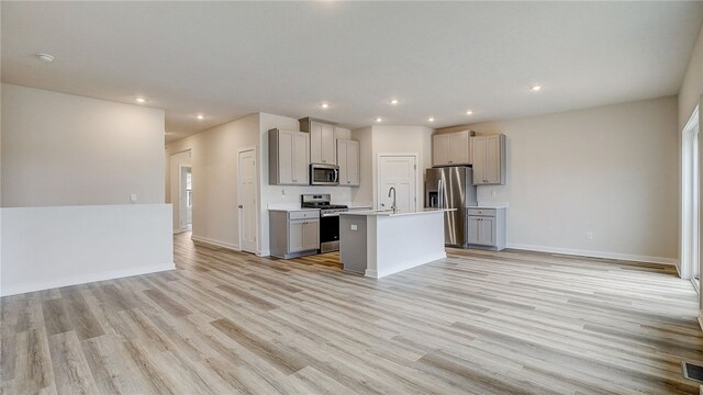 kitchen featuring light hardwood / wood-style floors, a center island with sink, gray cabinets, appliances with stainless steel finishes, and sink