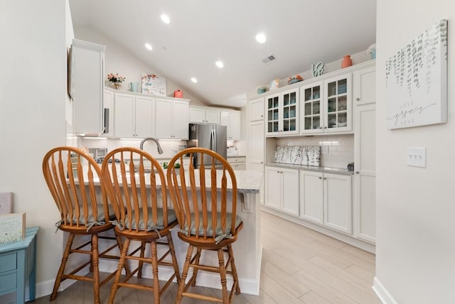 kitchen with white cabinets, light stone counters, backsplash, and stainless steel refrigerator