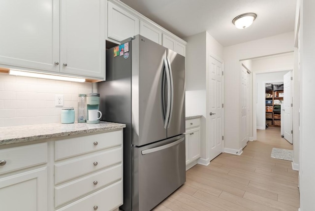 kitchen with stainless steel refrigerator, white cabinetry, light stone counters, light hardwood / wood-style flooring, and decorative backsplash