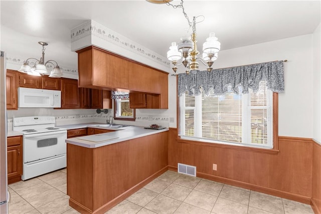 kitchen with an inviting chandelier, kitchen peninsula, wood walls, decorative light fixtures, and white appliances