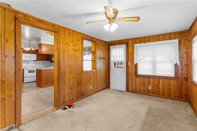 unfurnished living room featuring light carpet, wood walls, and ceiling fan with notable chandelier