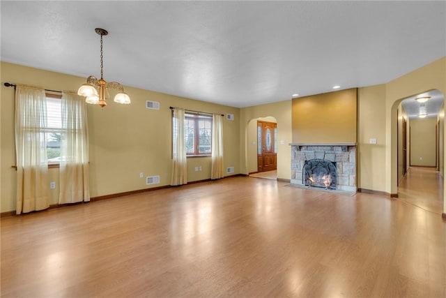 unfurnished living room with a stone fireplace, light hardwood / wood-style floors, and a notable chandelier