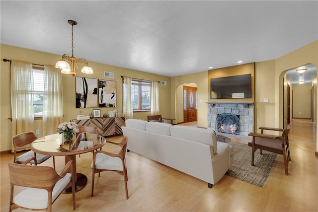 living room featuring a notable chandelier, light hardwood / wood-style floors, and a stone fireplace