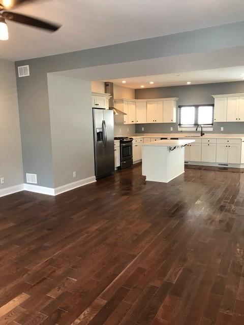 kitchen with white cabinetry, stainless steel fridge, black range oven, and a kitchen island