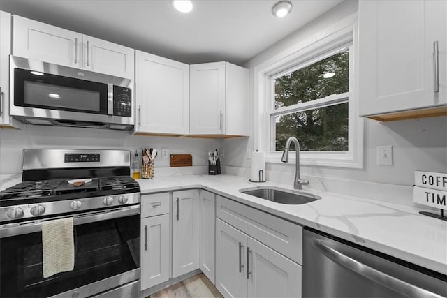 kitchen with sink, light stone countertops, light wood-type flooring, white cabinetry, and stainless steel appliances