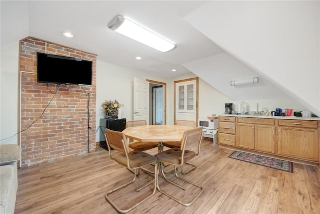 dining room featuring light hardwood / wood-style flooring, vaulted ceiling, and sink