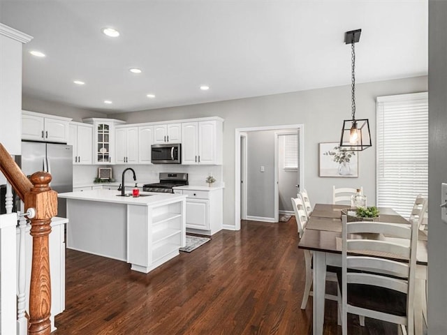 kitchen with stainless steel appliances, sink, white cabinets, hanging light fixtures, and an island with sink