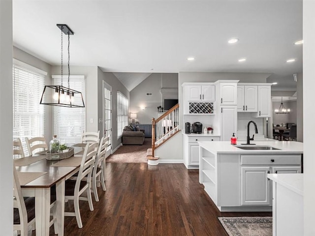 kitchen with dark hardwood / wood-style flooring, a kitchen island with sink, sink, white cabinets, and hanging light fixtures