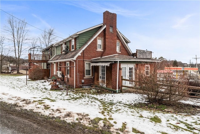 snow covered property featuring cooling unit, brick siding, and a chimney