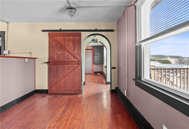 hall featuring a barn door, baseboards, arched walkways, and dark wood-type flooring