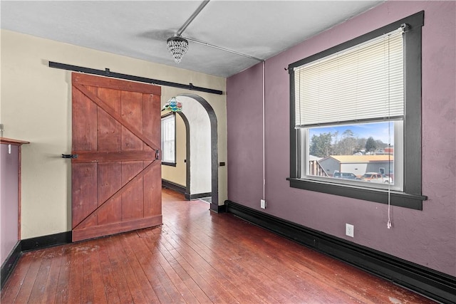 unfurnished room with baseboards, a barn door, arched walkways, and dark wood-type flooring