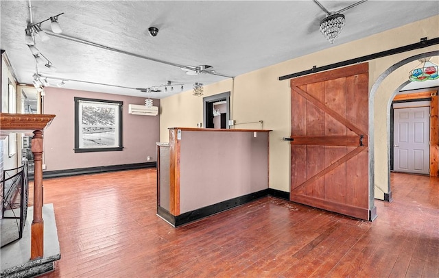 kitchen with a barn door, arched walkways, wood finished floors, decorative light fixtures, and an AC wall unit