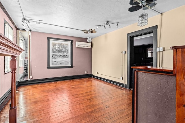 spare room featuring a textured ceiling, a wall unit AC, wood finished floors, and track lighting