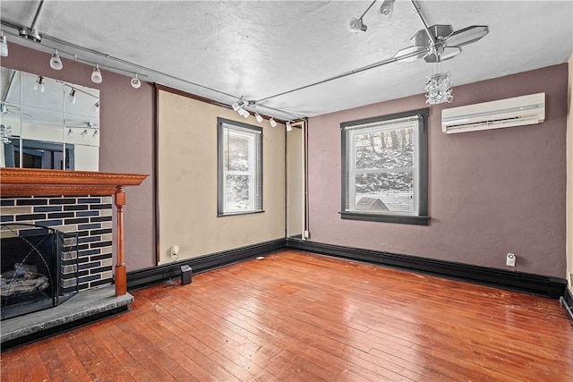 interior space featuring a fireplace with raised hearth, a wall mounted air conditioner, wood finished floors, and plenty of natural light